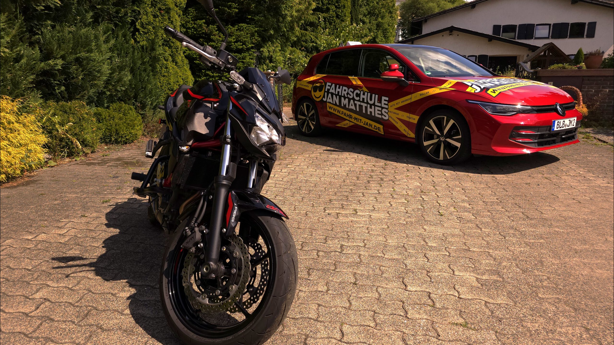 Schwarzes Kawasaki Z650 Motorrad im Vordergrund und rotes VW Golf 8 Fahrschulauto der Fahrschule Jan Matthes in Bad Berleburg