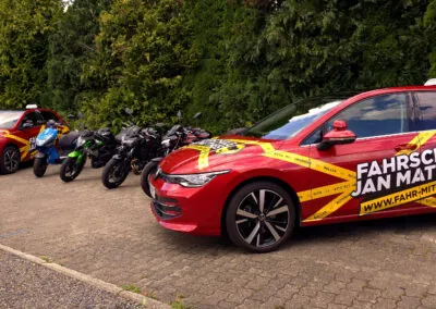 Der gesamte Fuhrpark der Fahrschule Jan Matthes in Bad Berleburg mit Autos, Motorrädern und einem Roller aufgereiht auf einem Parkplatz