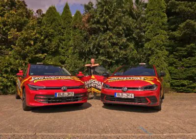 Fahrlehrer Jan Matthes steht zwischen zwei roten Fahrschulautos VW Golf und VW Polo der Fahrschule in Bad Berleburg