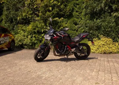 Schwarzes Kawasaki Z650 Motorrad neben einem Fahrschulauto der Fahrschule Jan Matthes in Bad Berleburg