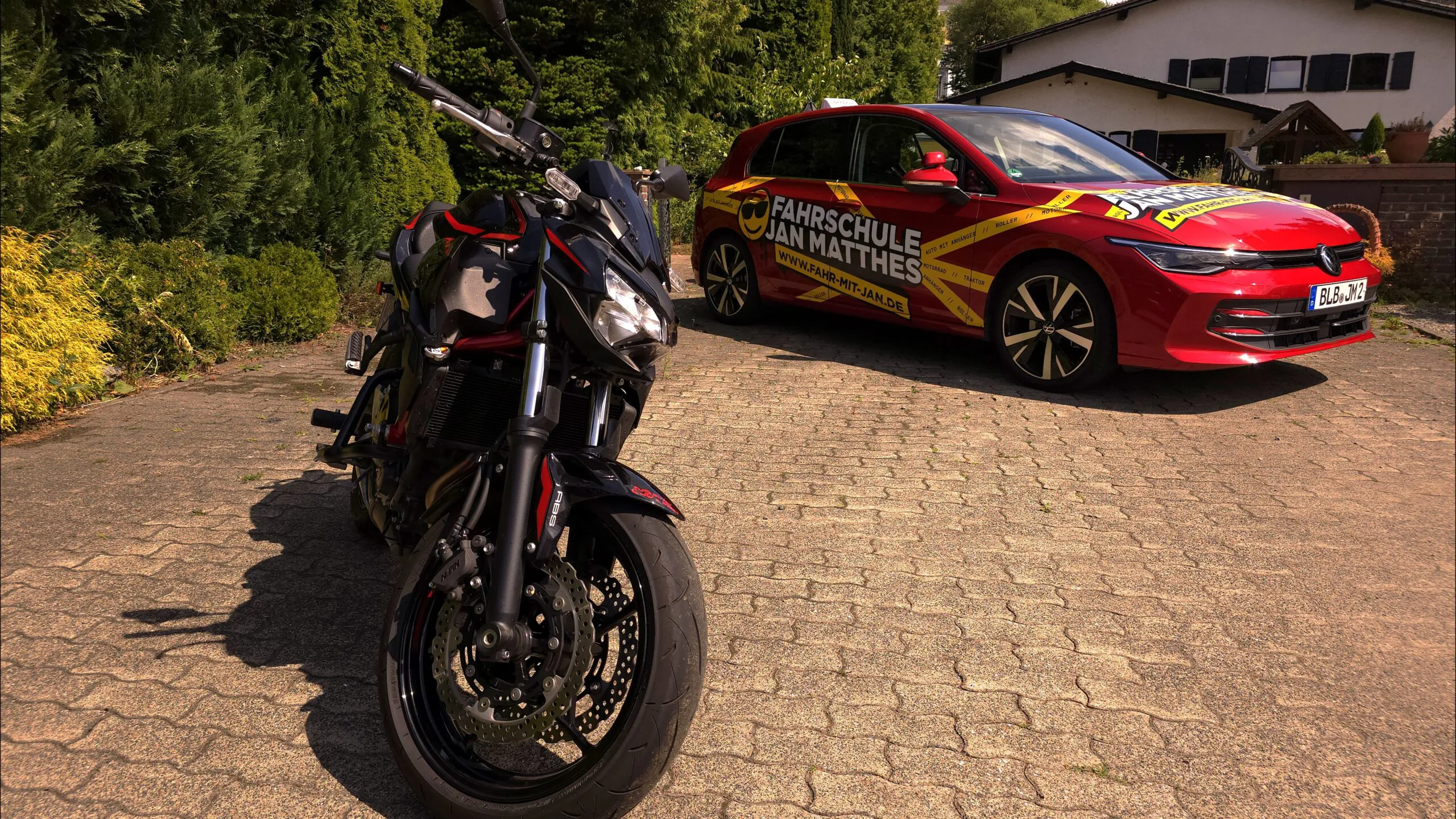 Schwarzes Kawasaki Z650 Motorrad im Vordergrund und rotes VW Golf 8 Fahrschulauto der Fahrschule Jan Matthes in Bad Berleburg