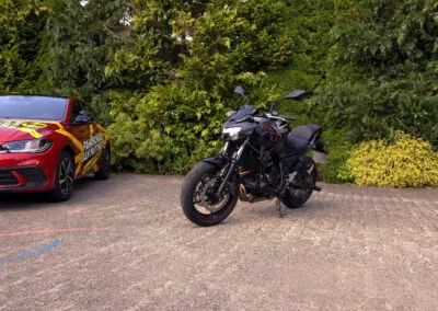 Schwarzes Kawasaki Z650 Motorrad neben einem roten VW Polo Fahrschulauto der Fahrschule Jan Matthes in Bad Berleburg